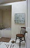 Blick auf Holzstuhl, im Hintergrund Badewanne teilweise sichtbar, schlichtes Bad mit Dielenboden, weiße abblätternde Farbe