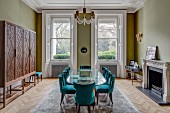 Oval glass table and petrol-blue upholstered chairs in grand dining room painted green
