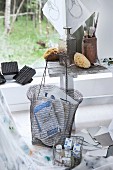 Art supplies in wire basket in front of paintbrushes and sponges on vintage wooden bank