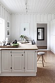 Kitchen counter with white base units in front of dining set in rustic interior with white wood-clad walls and cork flooring