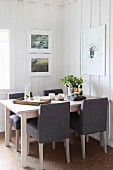 Dining area with grey upholstered chairs in rustic interior with white wood-clad walls