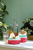 Gehäkelte Melonen-Körbchen mit Keksen neben Gläsern und Bügelflaschen auf Gartentisch