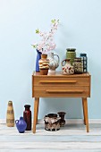 Retro ceramic vases on top of and beneath chest of drawers against wall painted pale blue