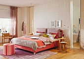 A feminine bedroom with a box spring bed in shades of red and gold patterned wallpaper