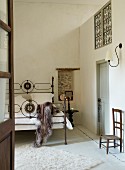 Antique iron bed, bedside table and wooden chair below sconce lamp in high-ceilinged bedroom