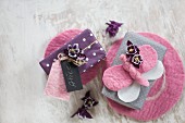 Verpackte Geschenke dekoriert mit Blüten, DIY-Geschenkanhänger und Filz-Schmetterling auf rosa Untersetzern