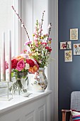 A bunch of different coloured roses in a glass vase and a bunch of flowers with carnations in a decorative vase