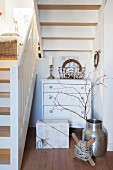 Festively decorated chest of drawers and wrapped gift below white wooden staircase