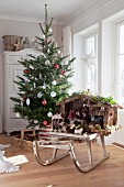 Geschmückter Weihnachtsbaum mit traditioneller Weihnachtskrippe auf Vintage Holzschlitten vor Sprossenfenstern