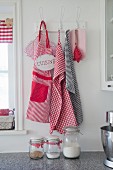 Red and white apron and tea towels hanging from vintage pegs with old-fashioned storage jars in foreground