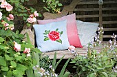 Romantic, knitted cushion cover with rose motif on rustic garden bench