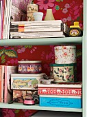 Magazines and vintage tins on shelving with back wall papered with red floral wallpaper