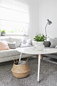 White coffee table and sofa with checked upholstery below window with closed roller blind