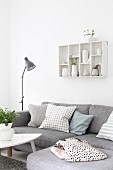 Grey corner sofa with scatter cushions below collection of vases in wall-mounted display case