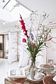Bunter Blumenstrauss mit Gladiole in Vase und Geschirr auf Tisch