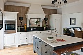 Island counter in white country-house kitchen with view into living area