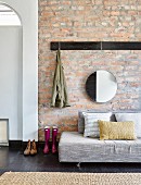Graues Sofa vor Backsteinwand mit Garderobe und rundem Spiegel