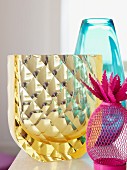 Collection of vases: pink wire container and yellow crystal vase in front of blue glass vase