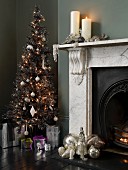 Christmas baubles on hearth and lit candles on mantelpiece next to decorated Christmas tree