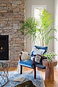 Reading corner with blue armchair in front of palm tree and brick fireplace