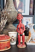 Red ethnic sculpture of woman next to animal figurine and beaker printed with Queen Elizabeth II motif