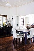 Elegant dining room with white upholstered chairs and black ethnic chest of drawers in front of a wall mirror