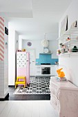 Rabbit ornament under glass cover on top of antique chest of drawers in front of open-plan kitchen with black and white cement floor tiles and pink fridge
