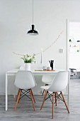 Classic chairs around white dining table below black pendant lamp