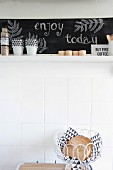 Bread basket in front of white wall tiles below kitchen shelf with chalkboard back wall