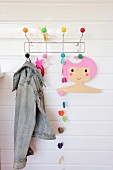 Colourful crocheted garland, denim jacket and coathanger with cartoon girl motif hung from coat rack
