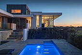 Pool outside contemporary house with illuminated interior at twilight