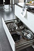 A kitchen island with an open drawer and a view of stainless steel pots