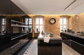 Moderne Küche mit schwarzen Hochglanzoberflächen und freistehenden Theken, Sandsteinwände mit indirekter Beleuchtung und abgehängte Decke