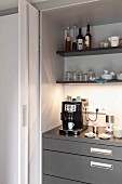 An open sliding door and a view of a kitchen cupboard with an espresso machine