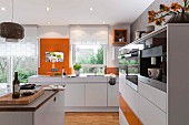 A modern, open-plan kitchen in white with orange accents