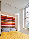 Fitted cupboards and striped headboard in small bedroom