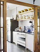 Cooker in white kitchen counter below pans on wooden shelf