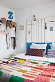 Colourful knitted patchwork blanket, headboard made from wooden boards and clothing hung from coat pegs in bedroom