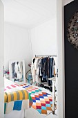 Colourful crocheted rug, clothes rack and mirror in bedroom