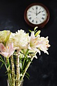 Exotischer Blumenstrauß vor schwarzer Wand mit Uhr