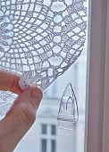 A transparent sticky hook on a window to hold a crocheted curtain