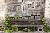 A weathered bench in front of an old, patched wooden gate