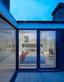 Twilight atmosphere over roof terrace with view into elegant modern bedroom