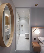 Round mirror in bedroom next to open door with view into illuminated minimalist bathroom