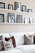 Scatter cushions in earthy tones on white sofa below pictures on narrow shelves