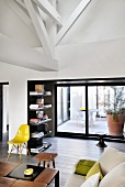 Sofa, designer coffee table, stool and classic yellow chair in front of shelves with conservatory behind glass sliding doors