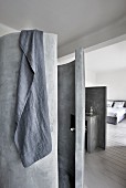 Grey towel hung over concrete cylindrical shower and view into bedroom
