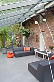 Wintergartenanbau an rustikaler Ziegelfassade mit grauen Designer-Loungemöbeln und orangefarbenen Farbakzenten