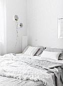 Crumpled pale grey bed linen in white bedroom