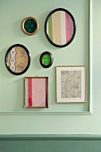 Assorted photo frames containing Biedermeier fabrics on a paste-green wall wth moulding